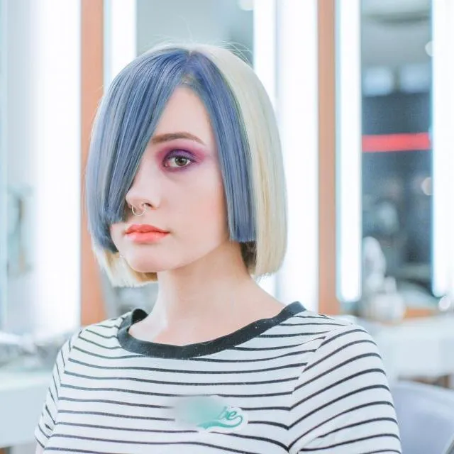 Une cliente à la coupe au carré gris-bleu, maquillée de rose, pose dans un salon de coiffure lumineux