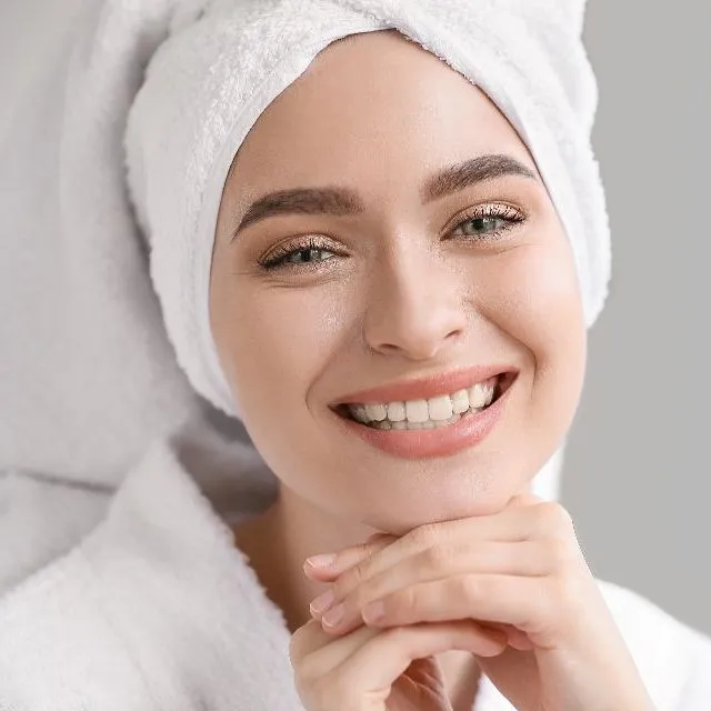A smiling client, her hair wrapped in a white towel, resting her chin on her hands