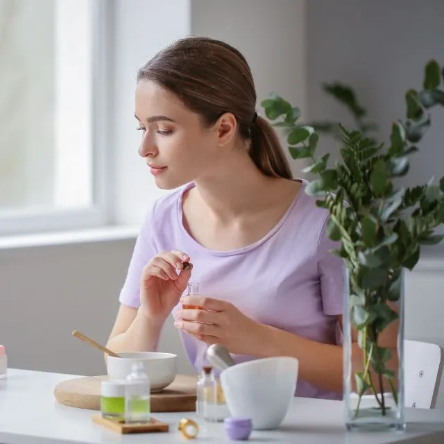 A beautician prepares a treatment on a white table: bowls, bottles and a dropper, next to a bunch of eucalyptus