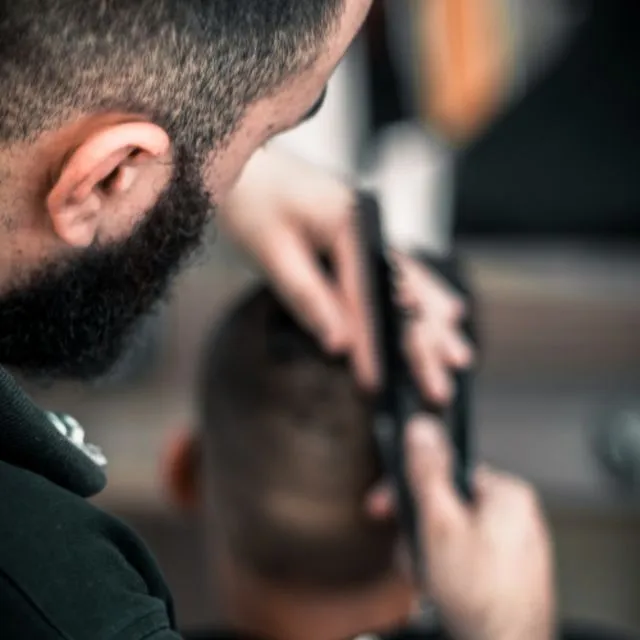 Un barbier dégrade la nuque d’un client à la tondeuse, dans la lumière chaude du salon