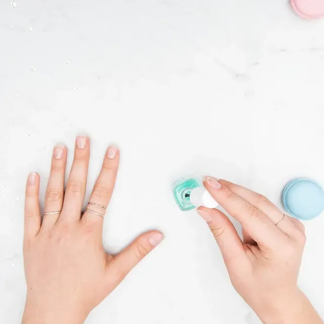Deux mains soignées sur une table de marbre clair, un flacon de vernis pastel ouvert